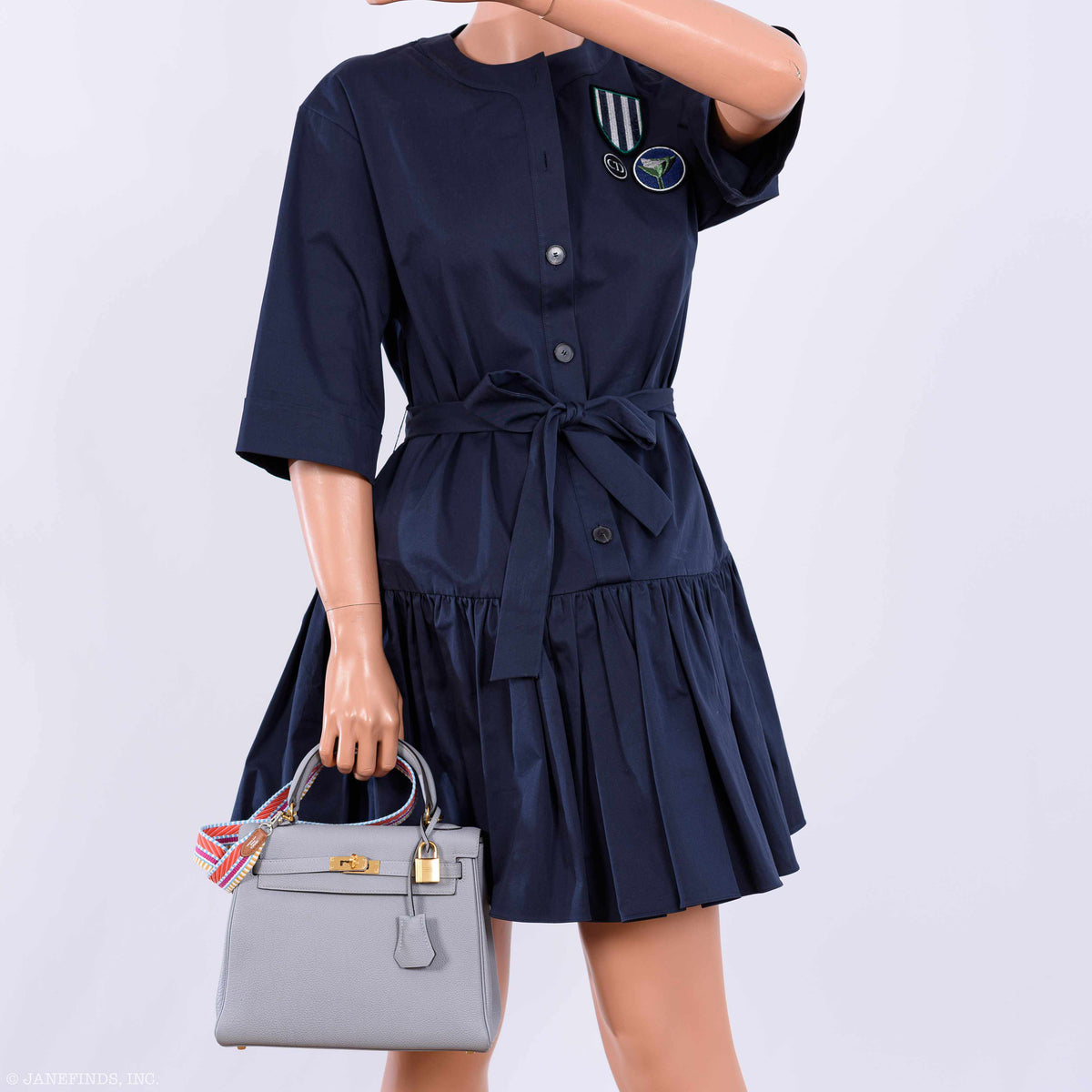 Navy dress worn by a mannequin holding a gray handbag on a white background